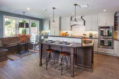 Example of a large classic l-shaped medium tone wood floor eat-in kitchen design in Los Angeles with a drop-in sink, shaker cabinets, white cabinets, granite countertops, white backsplash, subway tile backsplash, stainless steel appliances and an island