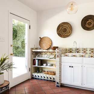 Ispirazione per una cucina parallela mediterranea con lavello da incasso, ante con riquadro incassato, ante bianche, top piastrellato, paraspruzzi beige, pavimento in terracotta, pavimento marrone e top beige