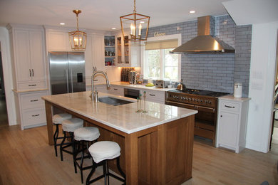 Inspiration for a large transitional l-shaped medium tone wood floor eat-in kitchen remodel in New York with a double-bowl sink, recessed-panel cabinets, gray cabinets, quartzite countertops, blue backsplash, subway tile backsplash, stainless steel appliances and an island