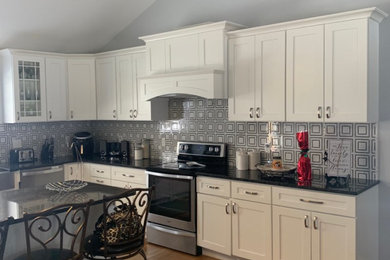 Inspiration for a mid-sized transitional l-shaped medium tone wood floor and brown floor eat-in kitchen remodel in Providence with a farmhouse sink, flat-panel cabinets, white cabinets, granite countertops, multicolored backsplash, cement tile backsplash, stainless steel appliances, an island and black countertops