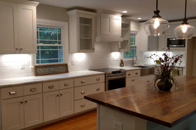 ローリーにある高級な中くらいなトランジショナルスタイルのおしゃれなキッチン (エプロンフロントシンク、シェーカースタイル扉のキャビネット、白いキャビネット、珪岩カウンター、白いキッチンパネル、サブウェイタイルのキッチンパネル、シルバーの調理設備、無垢フローリング、茶色い床、白いキッチンカウンター) の写真