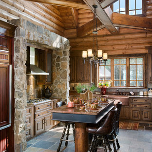 Country kitchen in Other with a farmhouse sink, raised-panel cabinets, panelled appliances, with island and slate splashback.