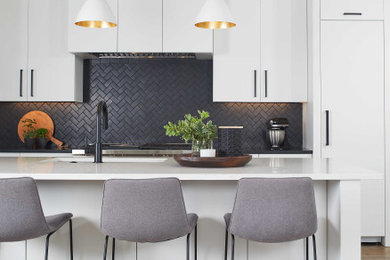 Mid-sized trendy galley light wood floor and brown floor open concept kitchen photo in Grand Rapids with an undermount sink, flat-panel cabinets, white cabinets, quartz countertops, black backsplash, ceramic backsplash, paneled appliances, an island and white countertops