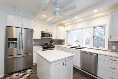 Example of a mid-sized transitional l-shaped slate floor kitchen design in Other with a double-bowl sink, flat-panel cabinets, white cabinets, solid surface countertops, gray backsplash, subway tile backsplash, stainless steel appliances and an island