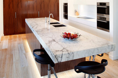 Immagine di una cucina contemporanea di medie dimensioni con lavello a doppia vasca, ante lisce, ante bianche, top in marmo, paraspruzzi bianco, elettrodomestici in acciaio inossidabile e parquet chiaro