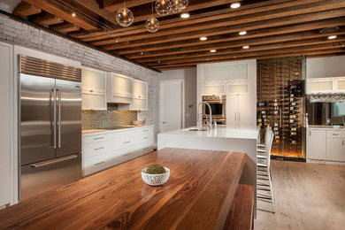 ボストンにあるインダストリアルスタイルのおしゃれなキッチン (フラットパネル扉のキャビネット、白いキャビネット、グレーのキッチンパネル、シルバーの調理設備、淡色無垢フローリング) の写真