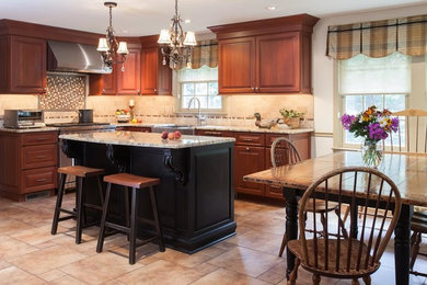 Inspiration for a mid-sized transitional l-shaped travertine floor eat-in kitchen remodel in Philadelphia with a farmhouse sink, raised-panel cabinets, medium tone wood cabinets, granite countertops, beige backsplash, stone tile backsplash, stainless steel appliances and an island