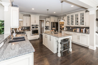 Inspiration for a large contemporary u-shaped dark wood floor and brown floor eat-in kitchen remodel in Cincinnati with a double-bowl sink, recessed-panel cabinets, white cabinets, granite countertops, gray backsplash, subway tile backsplash, stainless steel appliances and an island