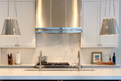 Foto på ett stort vintage vit kök, med en undermonterad diskho, luckor med infälld panel, vita skåp, bänkskiva i kvarts, vitt stänkskydd, stänkskydd i sten, rostfria vitvaror, mellanmörkt trägolv, en köksö och brunt golv