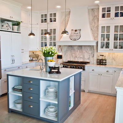 Example of a beach style u-shaped kitchen design in Seattle with paneled appliances, a farmhouse sink, glass-front cabinets, white cabinets, marble countertops, white backsplash and marble backsplash
