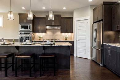 Inspiration for a mid-sized contemporary l-shaped medium tone wood floor and brown floor open concept kitchen remodel in Portland with a drop-in sink, flat-panel cabinets, dark wood cabinets, granite countertops, beige backsplash, ceramic backsplash, stainless steel appliances and an island