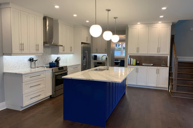 Mid-sized trendy single-wall medium tone wood floor and brown floor open concept kitchen photo in Other with an undermount sink, shaker cabinets, white cabinets, solid surface countertops, white backsplash, marble backsplash, stainless steel appliances, an island and white countertops