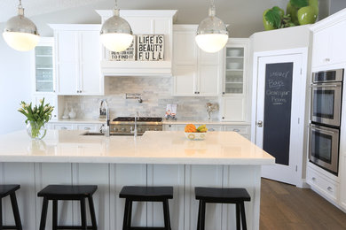 Inspiration for a mid-sized transitional l-shaped medium tone wood floor eat-in kitchen remodel in Edmonton with a farmhouse sink, recessed-panel cabinets, white cabinets, marble countertops, white backsplash, stone tile backsplash, stainless steel appliances and an island