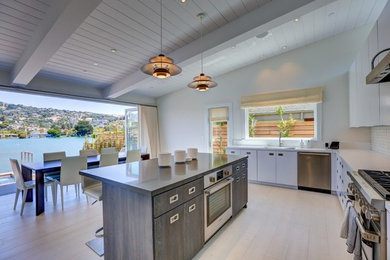 Example of a large trendy l-shaped light wood floor and white floor eat-in kitchen design in San Francisco with an undermount sink, flat-panel cabinets, white cabinets, white backsplash, stainless steel appliances, an island, solid surface countertops and stone tile backsplash