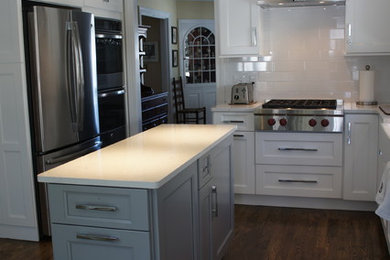 Small transitional l-shaped medium tone wood floor eat-in kitchen photo in Bridgeport with a farmhouse sink, shaker cabinets, white cabinets, quartz countertops, white backsplash, ceramic backsplash, stainless steel appliances and an island
