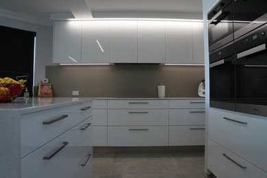 Inspiration for an expansive contemporary u-shaped open plan kitchen in Perth with a built-in sink, flat-panel cabinets, white cabinets, engineered stone countertops, grey splashback, glass sheet splashback, stainless steel appliances, cement flooring, an island, grey floors and white worktops.