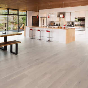 Idées déco pour une grand cuisine ouverte parallèle moderne avec un évier encastré, un placard à porte plane, des portes de placard blanches, un électroménager en acier inoxydable, un sol en bois clair, un îlot central et un sol beige.