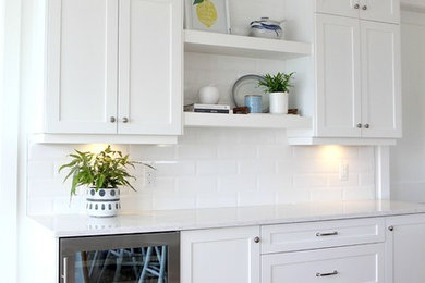Exempel på ett mellanstort klassiskt vit vitt kök, med en undermonterad diskho, skåp i shakerstil, vita skåp, bänkskiva i kvarts, vitt stänkskydd, stänkskydd i tunnelbanekakel, rostfria vitvaror, ljust trägolv och en köksö