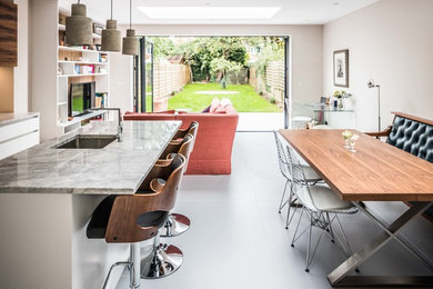 Inspiration for a medium sized contemporary l-shaped open plan kitchen in Oxfordshire with a single-bowl sink, flat-panel cabinets, white cabinets, granite worktops, metallic splashback, stainless steel appliances, ceramic flooring, a breakfast bar and grey floors.