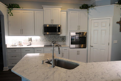 Example of a large transitional u-shaped dark wood floor and brown floor enclosed kitchen design in Jacksonville with an undermount sink, raised-panel cabinets, white cabinets, quartzite countertops, gray backsplash, mosaic tile backsplash, stainless steel appliances, a peninsula and white countertops