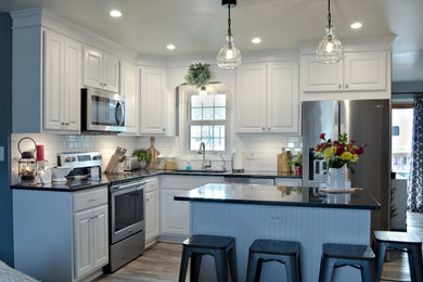 L-shaped kitchen photo in Other with raised-panel cabinets, white cabinets, granite countertops, white backsplash, stainless steel appliances, an island and black countertops