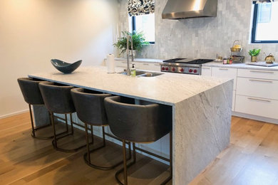 Photo of a large modern galley kitchen/diner in Richmond with a submerged sink, marble worktops, an island, flat-panel cabinets, white cabinets, grey splashback, marble splashback, stainless steel appliances, light hardwood flooring, beige floors and grey worktops.