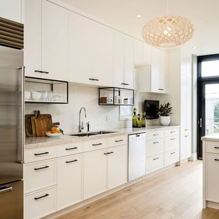 Design ideas for a large contemporary galley open plan kitchen in San Francisco with white cabinets, white splashback, stainless steel appliances, a double-bowl sink, shaker cabinets, solid surface benchtops, porcelain splashback and light hardwood floors.