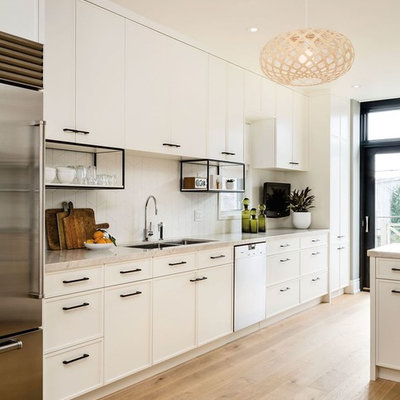 Open concept kitchen - large contemporary galley light wood floor open concept kitchen idea in San Francisco with white cabinets, white backsplash, stainless steel appliances, a double-bowl sink, shaker cabinets, solid surface countertops and porcelain backsplash