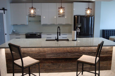 Example of a mid-sized trendy galley porcelain tile and gray floor eat-in kitchen design in Miami with a farmhouse sink, flat-panel cabinets, white cabinets, quartz countertops, white backsplash, glass tile backsplash, black appliances, an island and multicolored countertops