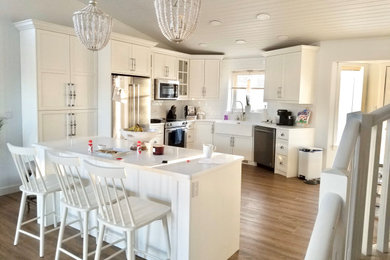 Inspiration for a contemporary l-shaped laminate floor eat-in kitchen remodel with a farmhouse sink, shaker cabinets, white cabinets, quartz countertops, white backsplash, ceramic backsplash, stainless steel appliances, an island and white countertops