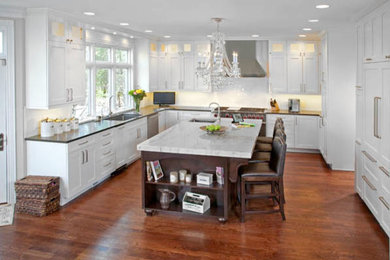 Mid-sized transitional l-shaped medium tone wood floor eat-in kitchen photo in Chicago with a farmhouse sink, recessed-panel cabinets, white cabinets, marble countertops, white backsplash, mosaic tile backsplash, stainless steel appliances and an island