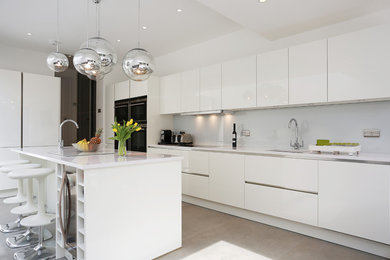 Inredning av ett modernt kök, med en enkel diskho, luckor med glaspanel, vita skåp, grått stänkskydd, glaspanel som stänkskydd, rostfria vitvaror och en köksö
