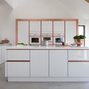 Inspiration for a contemporary u-shaped open plan kitchen in Other with a submerged sink, flat-panel cabinets, white cabinets, white splashback, integrated appliances, concrete flooring, an island, grey floors and white worktops.