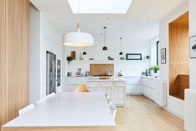 This is an example of a large contemporary u-shaped open plan kitchen in London with flat-panel cabinets, white cabinets, composite countertops, light hardwood flooring, an island, brown floors and white worktops.