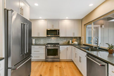 Inspiration for a mid-sized transitional u-shaped light wood floor and brown floor enclosed kitchen remodel in San Francisco with an undermount sink, shaker cabinets, white cabinets, quartz countertops, gray backsplash, stone tile backsplash, stainless steel appliances, no island and gray countertops