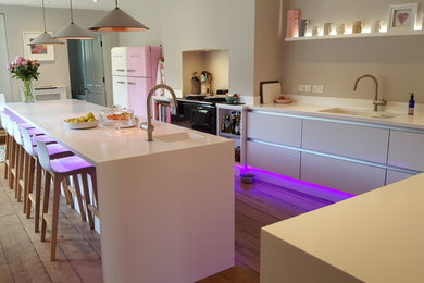 This is an example of a contemporary l-shaped kitchen in Hampshire with a built-in sink, glass-front cabinets, white cabinets, stainless steel appliances, medium hardwood flooring, a breakfast bar and brown floors.