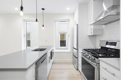 Example of a mid-sized minimalist single-wall light wood floor and brown floor eat-in kitchen design in New York with an undermount sink, flat-panel cabinets, white cabinets, solid surface countertops, white backsplash, subway tile backsplash, an island and gray countertops