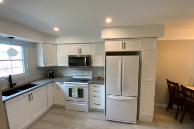 Example of a mid-sized transitional l-shaped vinyl floor and gray floor enclosed kitchen design in Other with a double-bowl sink, shaker cabinets, white cabinets, quartzite countertops, white backsplash, subway tile backsplash, white appliances, no island and gray countertops