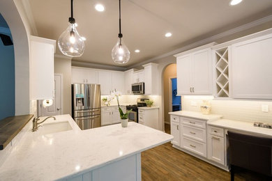 Inspiration for a mid-sized transitional u-shaped medium tone wood floor and brown floor eat-in kitchen remodel in Raleigh with an undermount sink, shaker cabinets, white cabinets, quartzite countertops, white backsplash, glass tile backsplash, stainless steel appliances and a peninsula