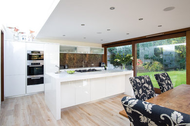 Diseño de cocina comedor contemporánea con armarios con paneles lisos, puertas de armario blancas, salpicadero marrón y salpicadero de losas de piedra