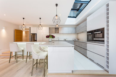 Photo of a large contemporary kitchen in London with a built-in sink, flat-panel cabinets, white cabinets, engineered stone countertops, beige splashback, ceramic splashback, ceramic flooring, an island and white floors.