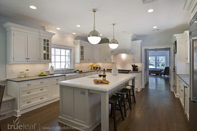 Inspiration for a transitional dark wood floor eat-in kitchen remodel in New York with a farmhouse sink, recessed-panel cabinets, white cabinets, marble countertops, white backsplash, ceramic backsplash, stainless steel appliances and an island