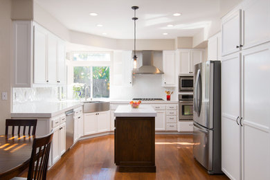 Foto de cocina contemporánea con fregadero de doble seno, puertas de armario blancas, electrodomésticos de acero inoxidable, una isla y suelo marrón