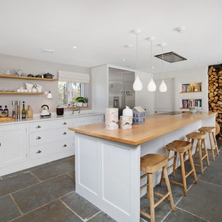 Design ideas for a coastal kitchen in Devon with a submerged sink, shaker cabinets, white cabinets, wood worktops, stainless steel appliances, an island, grey floors, beige worktops and slate flooring.