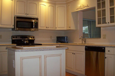 Küche mit Doppelwaschbecken, Schränken im Used-Look, Granit-Arbeitsplatte, Küchenrückwand in Weiß, Küchengeräten aus Edelstahl und braunem Holzboden in Orlando