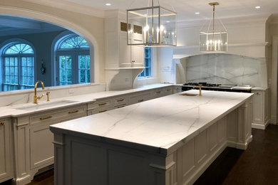 Inspiration for a large timeless u-shaped dark wood floor and brown floor eat-in kitchen remodel in New York with an undermount sink, recessed-panel cabinets, white cabinets, marble countertops, white backsplash, marble backsplash, paneled appliances, an island and white countertops