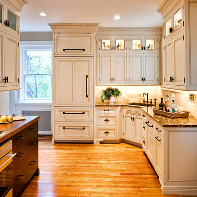 Mid-sized elegant l-shaped medium tone wood floor enclosed kitchen photo in St Louis with an integrated sink, recessed-panel cabinets, beige cabinets, beige backsplash, paneled appliances, granite countertops, stone tile backsplash and a peninsula