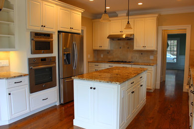 Klassisk inredning av ett mellanstort kök, med en undermonterad diskho, luckor med upphöjd panel, vita skåp, granitbänkskiva, beige stänkskydd, stänkskydd i porslinskakel, rostfria vitvaror, mellanmörkt trägolv, en köksö och brunt golv