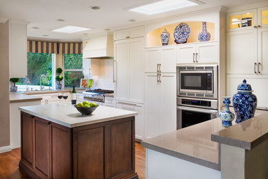 Inspiration for a large transitional u-shaped medium tone wood floor and brown floor eat-in kitchen remodel in San Diego with recessed-panel cabinets, white cabinets, white backsplash, subway tile backsplash, stainless steel appliances, an island, a double-bowl sink, quartz countertops and beige countertops
