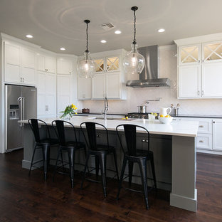 Modelo de cocina en L, clásica renovada, con fregadero bajoencimera, armarios estilo shaker, puertas de armario blancas, salpicadero blanco, suelo de madera oscura y una isla